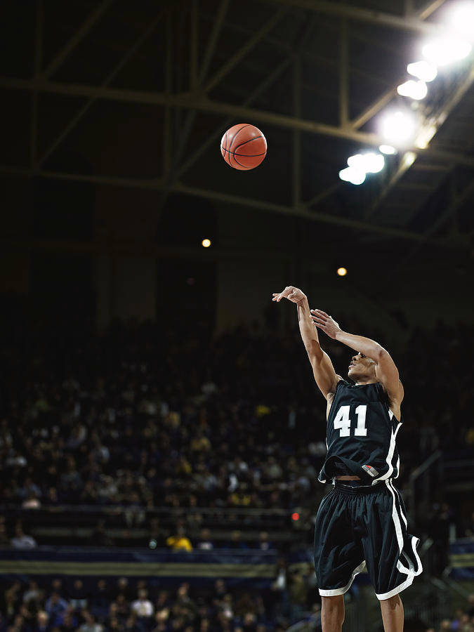 Basketball player taking a jump shot during a game in a packed arena